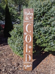 a wooden sign that says baby it's cold outside in front of some bushes