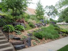 the steps lead up to a lush green hillside with rocks and plants on it's sides