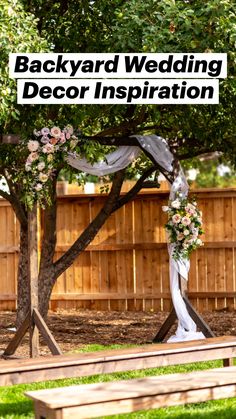 a wooden bench sitting under a tree with a white and pink wedding arch on it