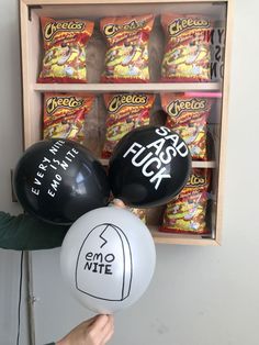 a person holding two black and white balloons in front of a shelf filled with snacks