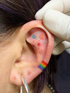 a woman getting her ear painted with rainbows and stars on the inside of it