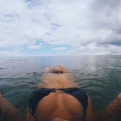 the back end of a person swimming in the ocean on a cloudy day with blue skies and white clouds