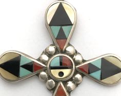 Acclaimed Zuni jewelers Zeno and Mary Ann Edaakie handcrafted this sterling silver and mosaic inlay cross with Sleeping Beauty turquoise, yellow mother of pearl, coral and jet. A Zuni Sunface is at the center of the cross. It hangs on a 26-inch chain. The back is signed ZME ZUNI NM. A word about inlay jewelry: It is best to remove inlay jewelry before bathing or showering. Do not wear inlay jewelry in hot tubs or pools. Avoid lotions, chemicals and prolonged exposure to water. The cross without Collectible Large Cross Pendant Jewelry, Handmade Southwestern Cross Pendant Jewelry, Handmade Southwestern Style Cross Pendant Jewelry, Southwestern Silver Cross Jewelry, Artisan Cross Jewelry For Jewelry Making, Handmade Multicolor Cross Jewelry, Collectible Cross-shaped Jewelry With Large Pendant, Collectible Cross Pendant Jewelry, Handmade Cross Jewelry Collectible