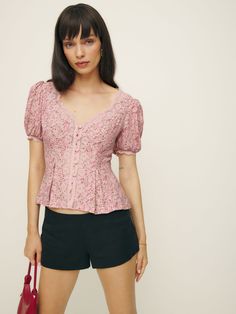 Up top. Shop the Minette Top from Reformation, a fitted top with a v-neckline, button front, short puffed sleeves, and lace detailing. Feminine V-neck Tops With Button Closure, Feminine V-neck Top With Button Closure, Feminine Fitted V-neck Blouse, Feminine Fitted V-neck Puff Sleeve Top, Spring Fitted V-neck Puff Sleeve Top, Fitted V-neck Puff Sleeve Top For Spring, Feminine Short Sleeve Puff Top, Feminine Puff Sleeve Top With Short Sleeves, Pink V-neck Puff Sleeve Top For Summer