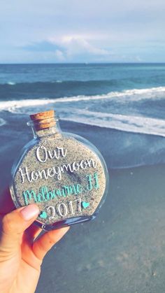 someone is holding up a bottle with the words on it and an ocean in the background