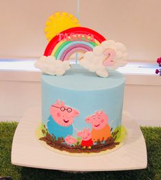 a birthday cake with peppa pig and rainbow decoration on top, sitting in the grass