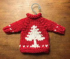 a red and white knitted sweater hanging from a hook on a wooden table,