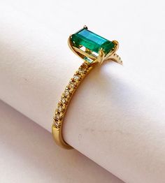 an emerald ring is sitting on top of a piece of white paper with gold trimmings