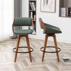 two wooden stools with green leather upholstered seats in front of a bookshelf