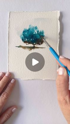 someone is painting a tree with watercolors on paper and using a blue brush