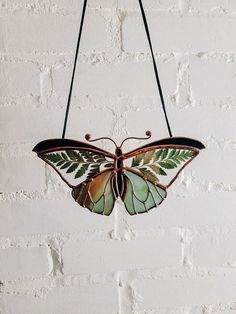 a green and brown butterfly hanging from a string on a brick wall next to a white brick wall