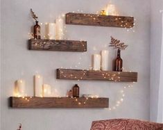 three wooden shelves filled with candles and some lights on top of each shelf in front of a white wall