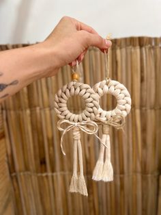 a person is holding up some tassels in front of a woven wall hanging