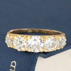 an antique five stone diamond ring sits on top of a blue velvet box with the word,