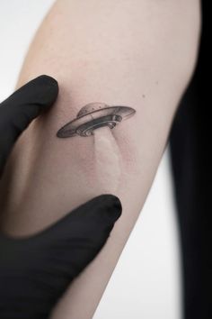 a person with a black glove on their arm holding up a tattoo that looks like a flying saucer