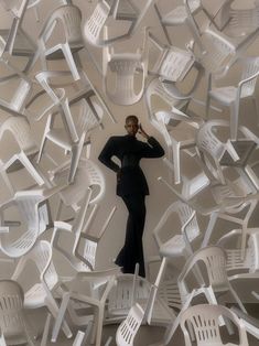 a woman standing in front of white chairs with one hand on her head and the other behind her