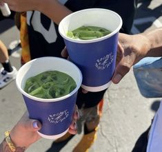 two people holding up cups filled with green beans