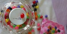 a glass jar filled with lots of colorful candies on top of a white table cloth