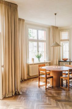 a dining room table and chairs in front of a large window with beige drapes