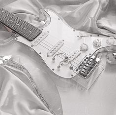 a black and white photo of an electric guitar on a silver sheeted surface with other accessories