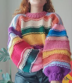 a doll is wearing a multicolored sweater and sitting in front of a plant