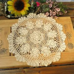 a doily is sitting on top of a wooden table next to a sunflower