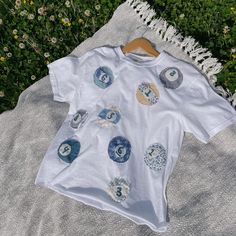 a white t - shirt with buttons on it sitting on a blanket in the grass