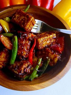 a wooden bowl filled with tofu, peppers and green beans next to yellow pepper