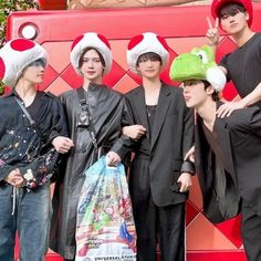 four people standing in front of a red wall wearing funny hats and holding a bag