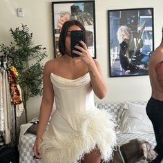 a woman taking a selfie in a white dress with ostrich feathers on it