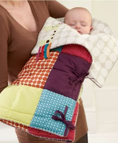 a woman holding a baby in a colorful quilted sling