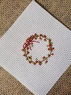 a white square with a red and green wreath on it sitting on top of a piece of cloth