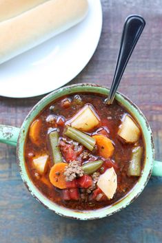 a bowl of soup with meat, vegetables and bread on a table next to a plate