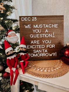 two elfs are sitting next to a sign that says, december 23 we must mustache you a question are you excited for santa tomorrow?