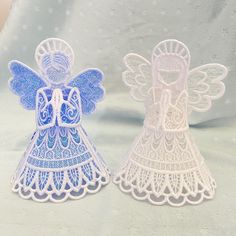 two paper angel figurines sitting next to each other on a white tablecloth