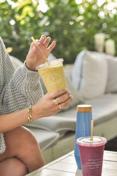 a woman sitting at a table with a drink in her hand and a straw in her other hand