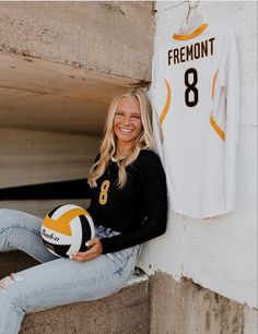 a woman holding a volleyball in her right hand and smiling at the camera while leaning against a wall