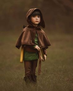 a little boy dressed up in a brown cloak and holding a yellow stick while standing in the grass