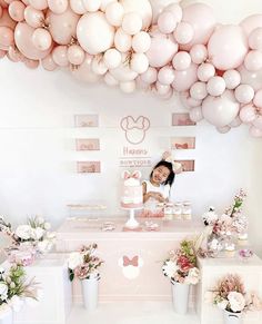 a woman standing behind a table with pink and white balloons