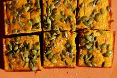 several squares of food with pumpkin and seeds on them sitting on an orange table top