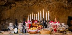 a table topped with lots of wine glasses and plates filled with food next to candles