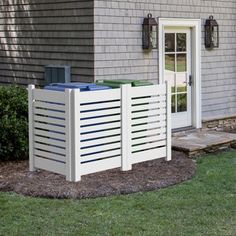 a white fence is in front of a house with a blue trash can on it