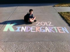 a young boy sitting on the sidewalk with chalk writing