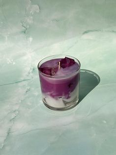 a purple candle sitting on top of a white counter next to a glass filled with liquid