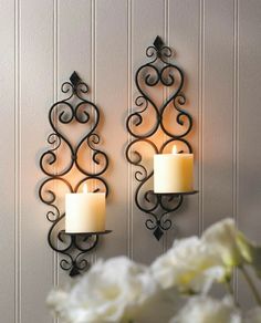 two wall sconces with candles on them in front of a white flower vase