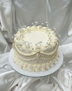 a three layer cake with white frosting flowers and pearls on the top is sitting on a plate