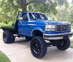 a blue pick up truck parked on top of a sidewalk in front of some trees