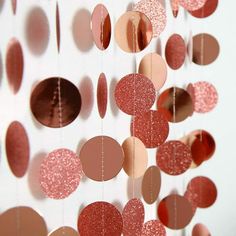 some pink and red circles are hanging from a string on a white wall with silver foil