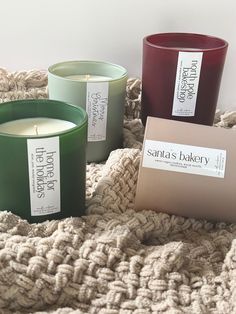 three candles sitting on top of a bed next to a box with the label santa's bakery