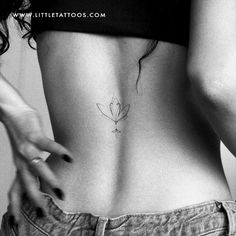 a woman's lower back with a small flower tattoo on her left side ribcage